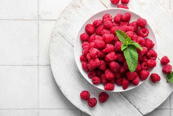 Bowl with fresh raspberries and mint on white tile table - Φωτογραφία, εικόνα