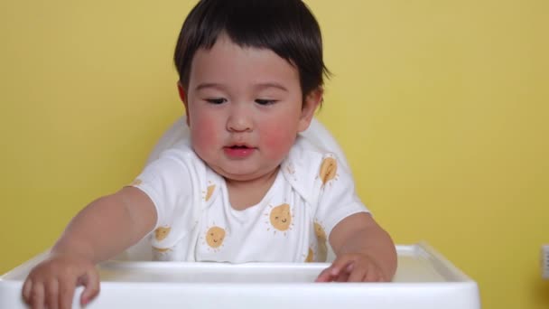 Lindo bebé asiático se sienta en la trona sobre fondo amarillo. Imágenes de alta calidad 4k - Imágenes, Vídeo