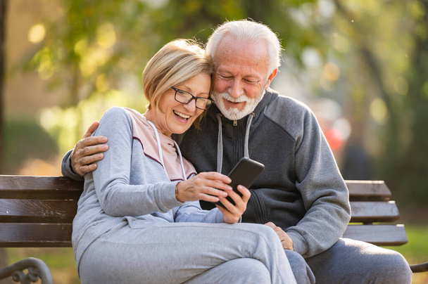 pareja de ancianos utilizando el teléfono móvil sentado en el banco en el parque - Foto, Imagen