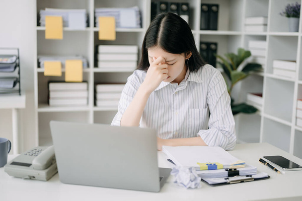 Asian woman feeling migraine head strain.Overworked businesswoman financier while working on laptop at office. - Fotó, kép