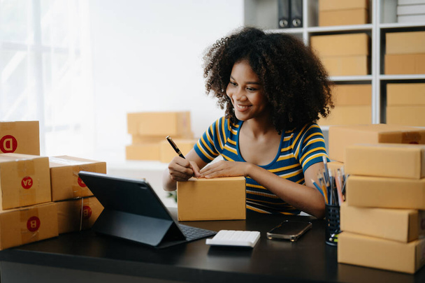 Small business entrepreneur SME freelance African woman working at home office with boxes and tablet , e-commerce concept - 写真・画像
