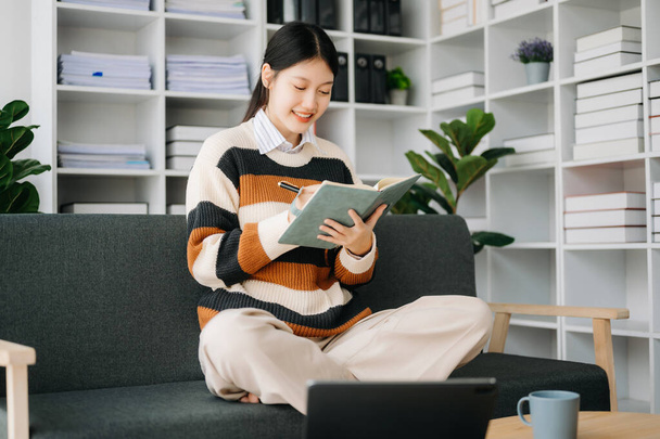 Fiduciosa donna asiatica con blocco note in soggiorno sul divano a casa ufficio - Foto, immagini