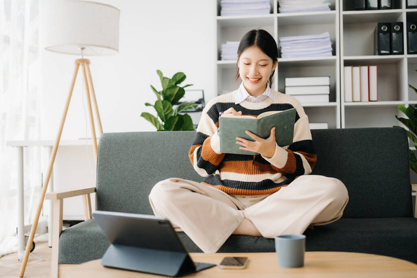 Confident Asian woman with  notepad and tablet pc in living room on the sofa at home office - Foto, afbeelding