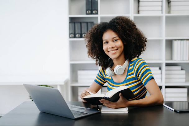  Женщина-студентка, африканская девушка, сидящая за столом с помощью ноутбука и книги - Фото, изображение