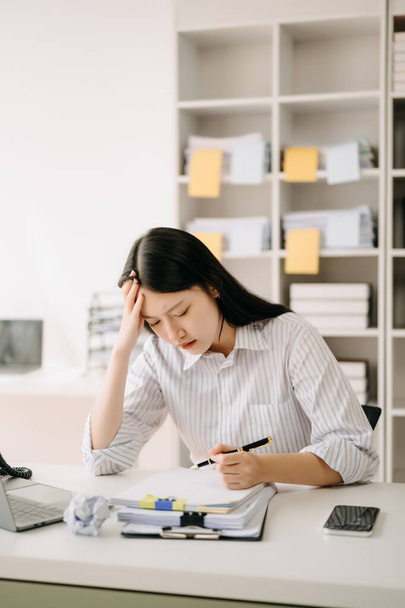 Asian woman feeling migraine head strain.Overworked businesswoman financier while working on laptop at office. - Foto, imagen