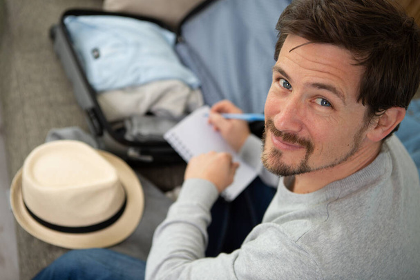 handsome bearded smiling man packing stuff holding check list - Fotografie, Obrázek