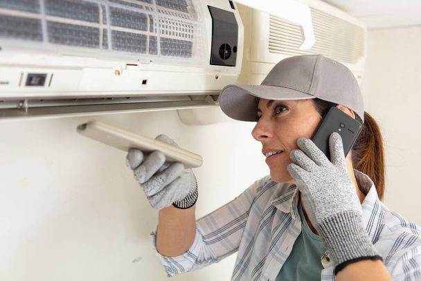 female technician repairing air conditioner and talking on telephone - Fotoğraf, Görsel