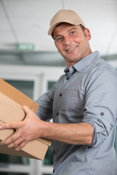 delivery man smiling and holding a cardboard box - Foto, afbeelding