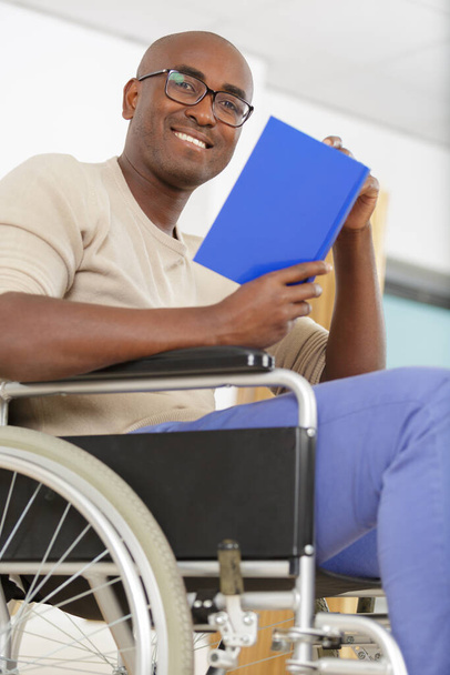 smiling physically handicapped man on wheelchair with book - Foto, imagen