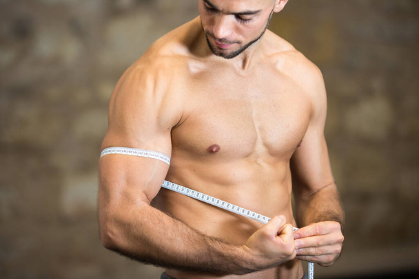 Muscular joven culturista hombre que mide bíceps con cinta
 - Foto, Imagen