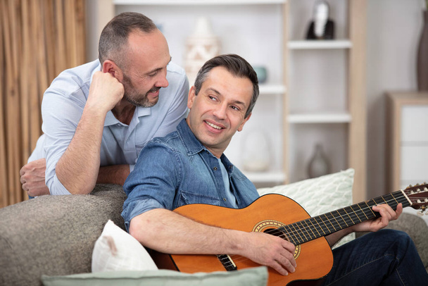a couple sitting on sofa and playing guitar at home - Foto, afbeelding