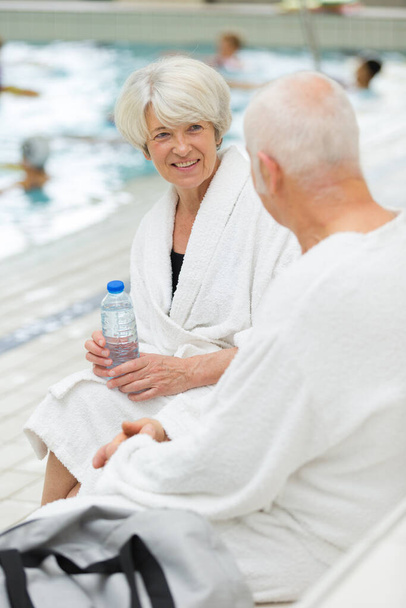 senior couple in bathrobes sat resting by the pool - Foto, Imagen