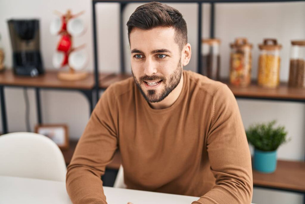 Jeune homme hispanique souriant confiant assis sur la table à la maison - Photo, image