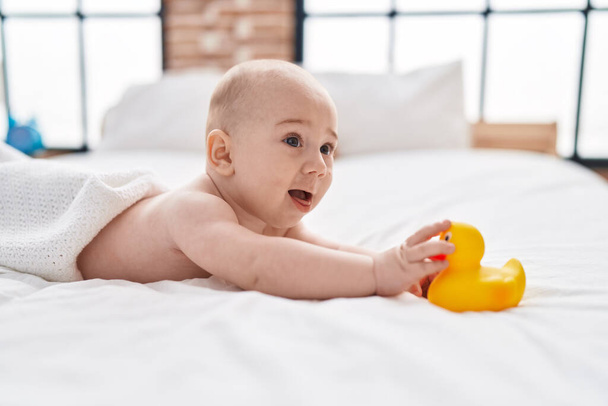 Adorável bebê caucasiano deitado na cama segurando brinquedo de pato no quarto - Foto, Imagem