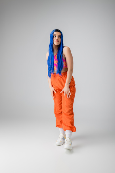 Mode-Statement, tätowierte junge Frau mit blauen Haaren posiert in bunten Kleidern auf grauem Hintergrund, volle Länge, Individualismus, modernen Stil, urbane Mode, lebendige Farbe, Modell  - Foto, Bild
