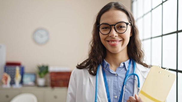 Mladá krásná hispánská žena lékař usměvavý jistý stojící na klinice - Fotografie, Obrázek