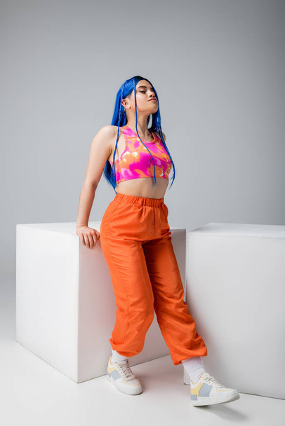 fashion trends, tattooed young woman with blue hair posing in colorful clothes near white cubes on grey background, full length, individualism, modern style, urban fashion, vibrant color, model  - Photo, Image