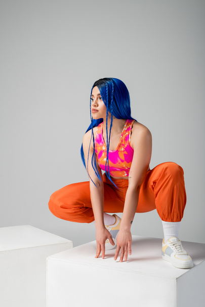 moda e stile, giovane donna tatuata con i capelli blu seduta sopra il cubo bianco su sfondo grigio, lunghezza intera, individualismo, stile moderno, moda urbana, colore vivace, modello  - Foto, immagini