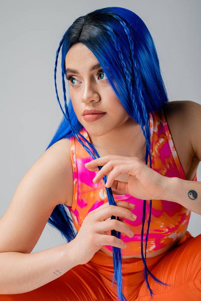 lázadó stílus, tetovált fiatal nő kék hajjal pózol színes ruhákban elszigetelt szürke háttér, stílusos megjelenés, félrenéz, modern egyéni, városi divat, generáció z  - Fotó, kép