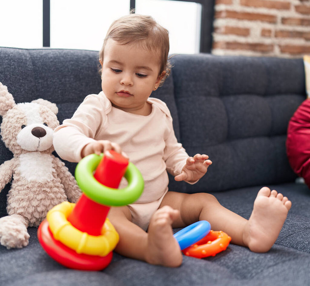 Adorable bebé hispano jugando con aros juego sentado en el sofá en casa - Foto, imagen