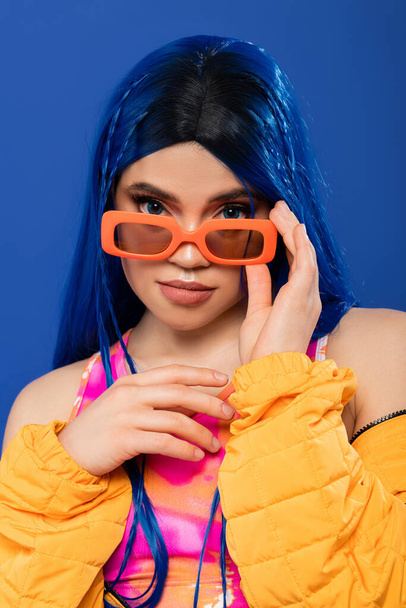fashion and style, young female model with blue hair and braids wearing trendy sunglasses isolated on blue background, generation z, rebel style, individualism, modern woman looking at camera - Foto, Bild