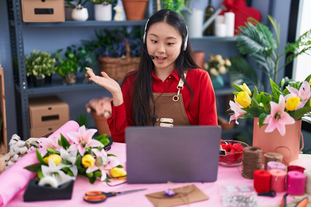 Молода азіатка, яка працює в магазині флористів, робить відеодзвінок, святкуючи досягнення з щасливою посмішкою і виразом переможця з піднятою рукою  - Фото, зображення