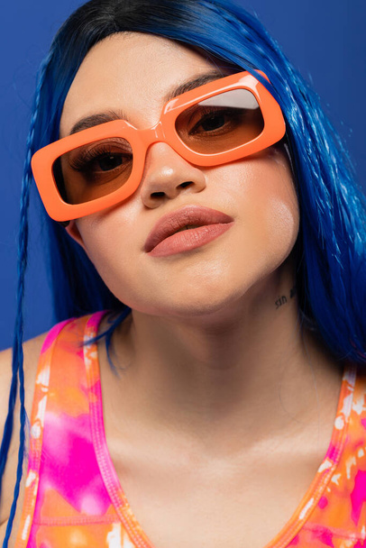 retrato, accesorio de moda, modelo femenino joven con pelo azul y gafas de sol de moda aisladas sobre fondo azul, generación z, estilo rebelde, estilo rebelde, individualismo, mujer moderna  - Foto, imagen