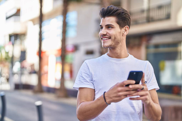 Young hispanic man smiling confident using smartphone at street - Zdjęcie, obraz