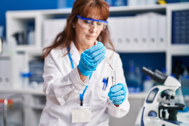 Middelbare leeftijd vrouw wetenschapper meten vloeistof in het laboratorium - Foto, afbeelding