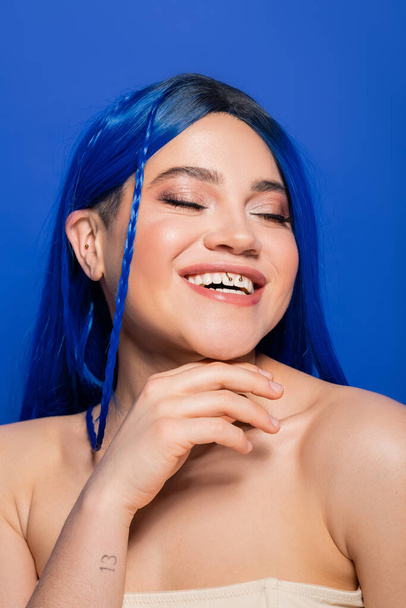 beauty concept, happy young woman with dyed hair posing on blue background, hair color, individualism, female model with makeup and trendy hairstyle smiling with closed eyes, vibrant youth  - Fotografie, Obrázek