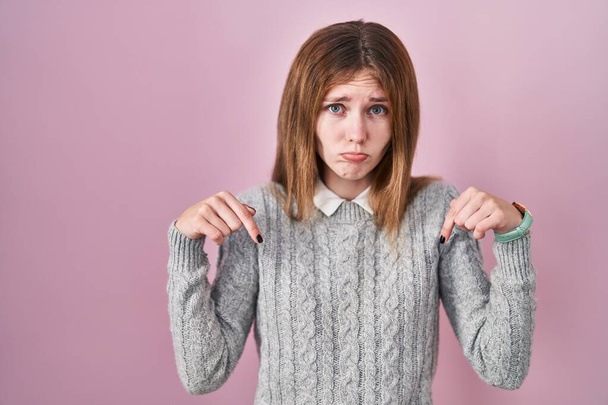 Beautiful woman standing over pink background pointing down looking sad and upset, indicating direction with fingers, unhappy and depressed.  - Foto, Imagem
