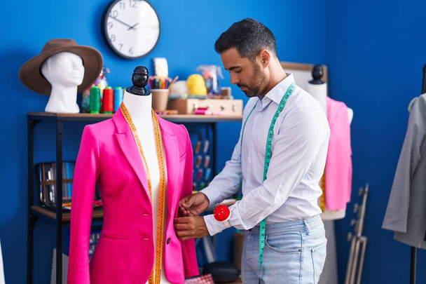 Young hispanic man tailor measuring jacket at sewing studio - 写真・画像