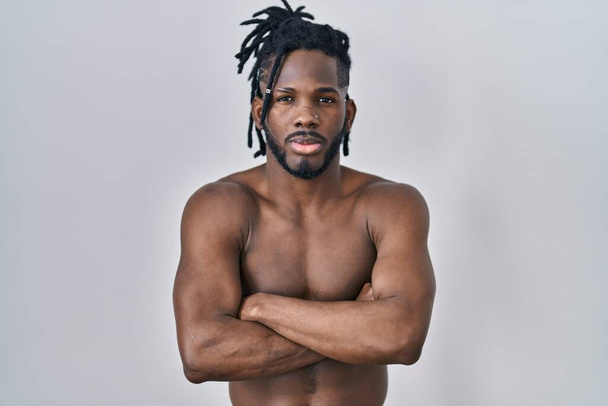 African man with dreadlocks standing shirtless over isolated background skeptic and nervous, disapproving expression on face with crossed arms. negative person.  - Fotografie, Obrázek