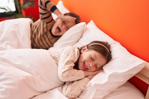 Schattige jongen en meisje glimlachen zelfverzekerd liggend op bed in de slaapkamer - Foto, afbeelding