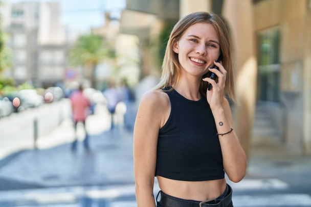 Nuori blondi nainen hymyilee luottavainen puhuu älypuhelimeen kadulla - Valokuva, kuva