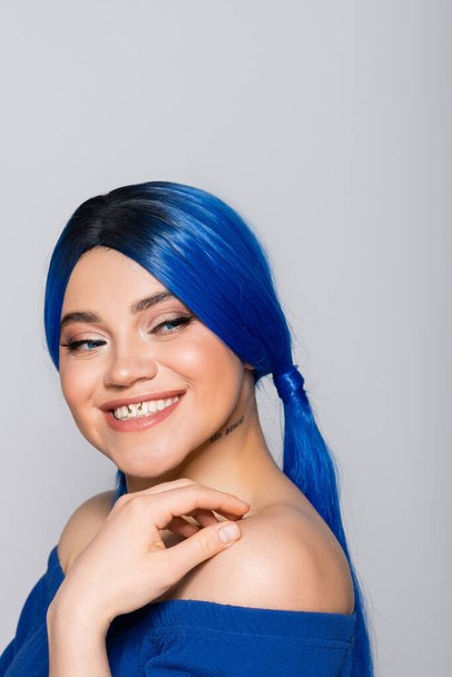 beauty trends, dyed hair, portrait of tattooed and cheerful woman with bare shoulders posing in bright blouse on grey background, blue hair color, hairstyle, female model, makeup and beauty  - Φωτογραφία, εικόνα