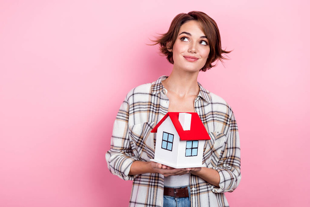 Portrait of lovely positive minded person hold little house look empty space isolated on pink color background. - 写真・画像