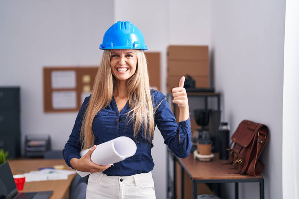 Young woman wearing architect hardhat smiling happy and positive, thumb up doing excellent and approval sign  - Foto, afbeelding