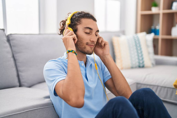 Молодой латиноамериканец слушает музыку, сидя дома на полу - Фото, изображение