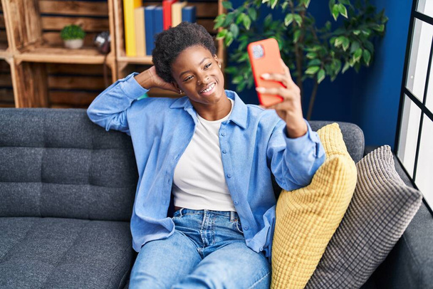 Afro-Amerikaanse vrouw het maken van selfie door de smartphone zitten op de bank thuis - Foto, afbeelding