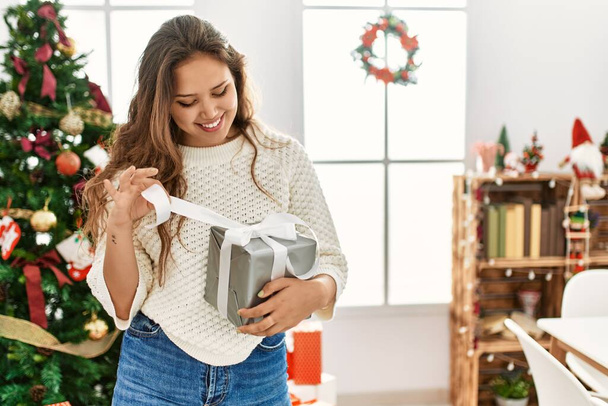 Jeune belle femme hispanique souriant confiant déballer cadeau de Noël à la maison - Photo, image