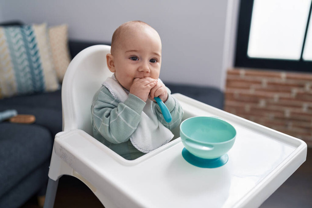 Adorabile caucasico bambino seduto sul seggiolone succhiare cucchiaio a casa - Foto, immagini