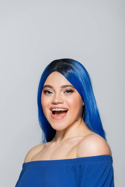 excitação e juventude, mulher tatuada com olhos azuis e cabelos tingidos sorrindo em fundo cinza, penteado, cabelo azul, beleza moderna, auto-expressão, individualismo  - Foto, Imagem