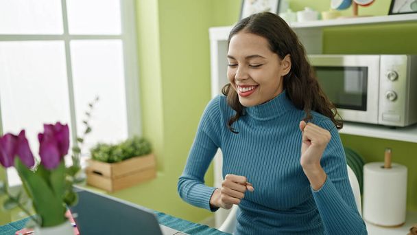 Νεαρή όμορφη ισπανόφωνη γυναίκα που χρησιμοποιεί φορητό υπολογιστή χορεύει στο σπίτι - Φωτογραφία, εικόνα