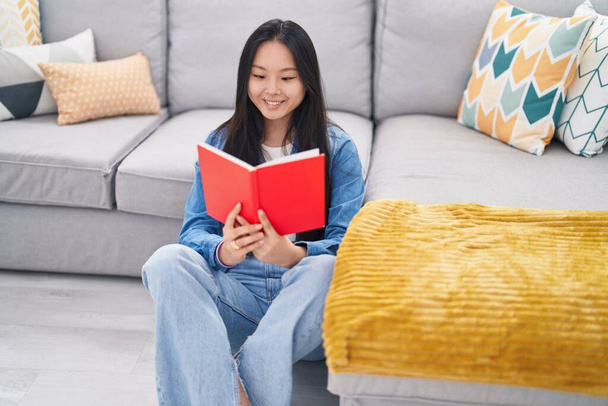 Joven mujer china leyendo libro sentado en el suelo en casa - Foto, imagen