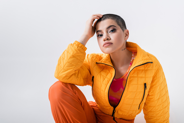 urban fashion, outerwear, female model posing in casual attire, young woman with short hair and puffer jacket sitting on grey background, looking at camera, personal style, self expression  - Foto, afbeelding