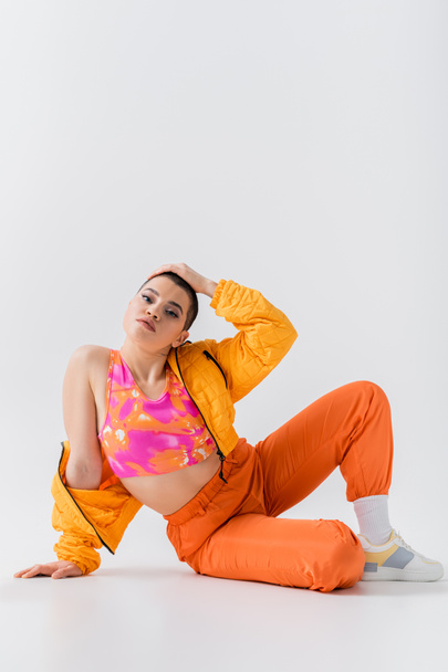 vibrant colors, tattooed young woman with short hair sitting on grey background, generation z, fashion forward, colorful clothes, female model with personal style, self expression, trendy outfit  - Foto, immagini