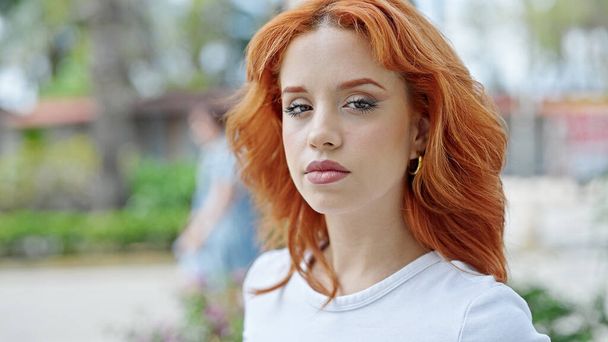 Young redhead woman standing with relaxed expression at park - Photo, Image