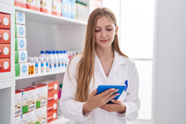 Young caucasian woman pharmacist using touchpad working at pharmacy - Foto, imagen