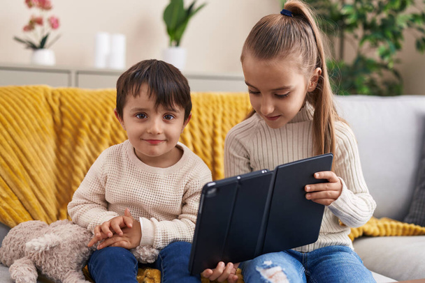 Adorable boy and girl using touchpad sitting on sofa at home - Zdjęcie, obraz